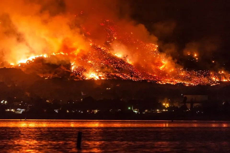 Wildfire burning at night on hillsides next to Lake Elsinore, California.